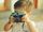 Ein blondes kleines Kind mit weißem Shirt hält alte analoge Kamera vor sein Gesicht
