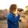 Eine junge Frau in Jeansjacke filmt durch eine altmodische Kamera mit der Sonne im Rücken