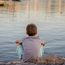 Ein Junge sitzt an einem Ufer und blickt auf das Wasser.