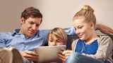 Vater, Tochter und Sohn sitzen auf der Couch und schauen auf ein Tablet