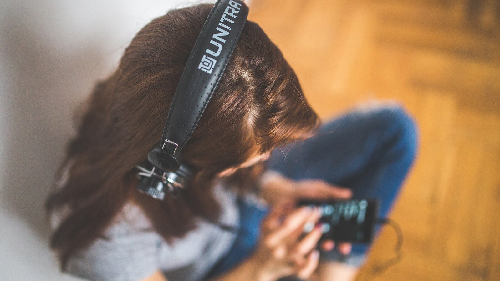 Eine Frau mit Kopfhoerern schaut etwas auf ihrem Smartphone