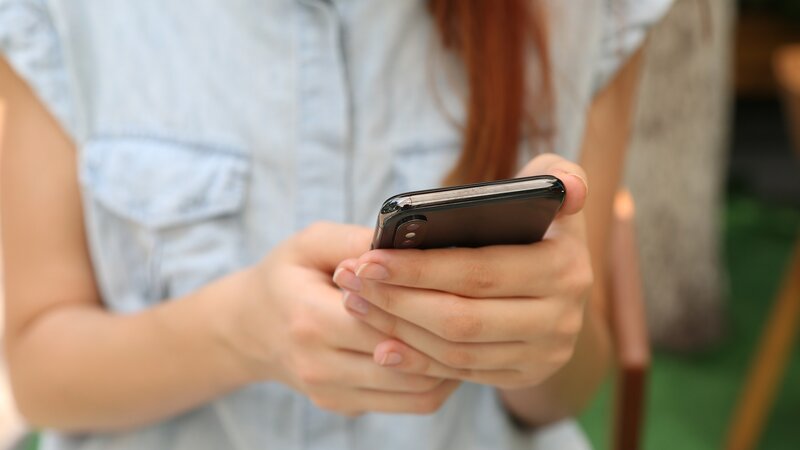 Eine junge Frau hält ein Smartphone in den Händen