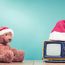 Ein Teddy mit Weihnachtsmütze sitzt vor gelbem Fernseher mit Weihnachtsmütze