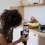 Auf einem Stativ steht ein Handy zum Filmen aufgestellt. Daneben ein Mädchen, dass die Videoaufnahme startet.
