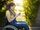 Eine junge Frau mit Dreadlocks sitzt im Rollstuhl in einem Park und schaut auf ihr Smartphone