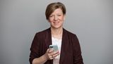 Portrait von Mediencoach Iren Schulz. Sie lächelt in die Kamera, während sie ein Smartphone in der Hand hält.
