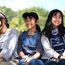Drei asiatische Mädchen sitzen nebeneinander auf einer Bank und lachen.