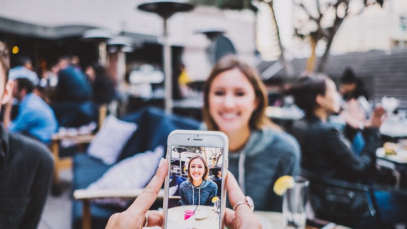 Jemand macht ein Foto einer jungen Frau mit dem Smartphone
