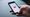 Hand hält Smartphone mit YouTube-Logo auf dem Bildschirm, grauer Hintergrund