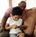 Ein Schwarzer Mann und sein Kind sitzen auf einer Couch und schauen auf ein Smartphone, das das Kind in den Händen hält