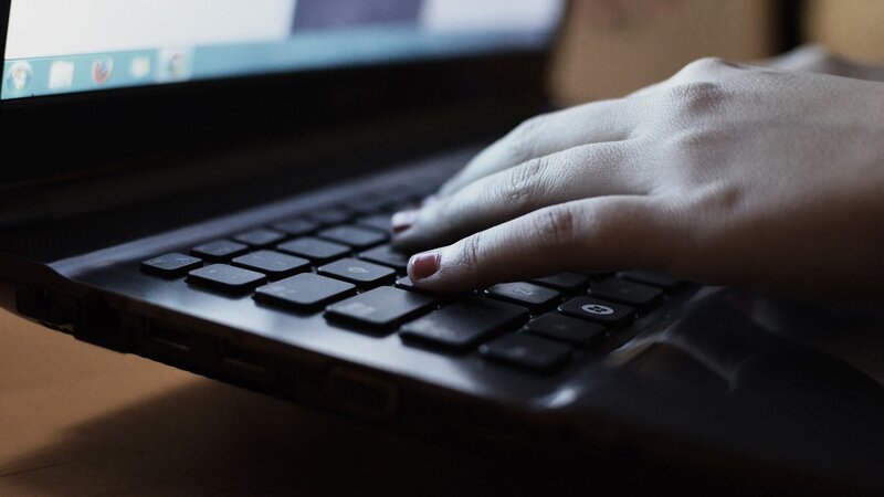 Eine Hand mit lackierten Fingernägeln tippt etwas auf dem Windows-Laptop