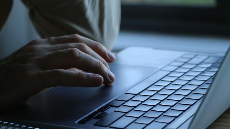 Ein Laptop steht auf einem Tisch, während eine Hand das Touchpad bedient. 