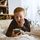 Ein Junge liegt auf dem Bett, schlägt die Hand an seine Wange und schaut überrascht in ein Smartphone