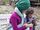 Eine Mutter mit Kopftuch sitzt auf der Parkbank und sieht auf ein Kind, das ein Smartphone in der Hand hält.