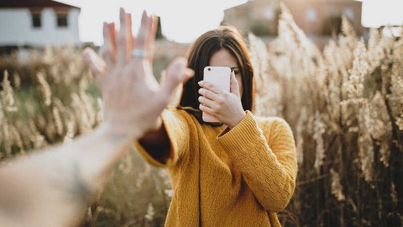 Zwei Teenager stehen sich gegenüber und halten ihre Händer aneinander. Das Mädchen gegenüber der Kamera hält ein Smartphone vor dem Gesicht