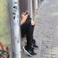 hinter einer Wand mit Graffiti sitzt eine jugendliche Person, von der man nur die Beine in zerrissenen Jeans und Sneakers und die Hände mit einem Smartphone sieht.