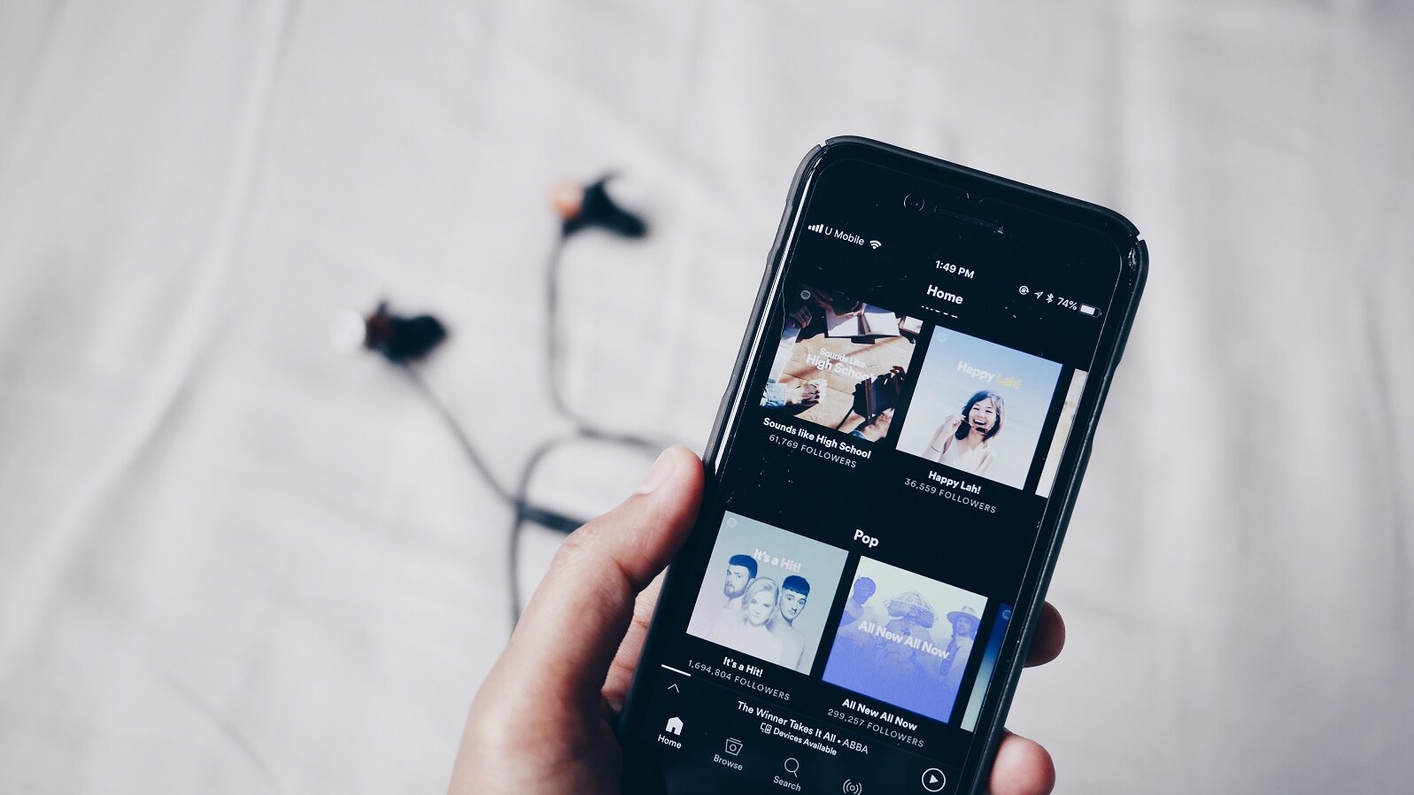 Ein Smartphone in einer Hand, auf dem Spotify geöffnet ist und Kopfhöhrer angeschlossen sind.