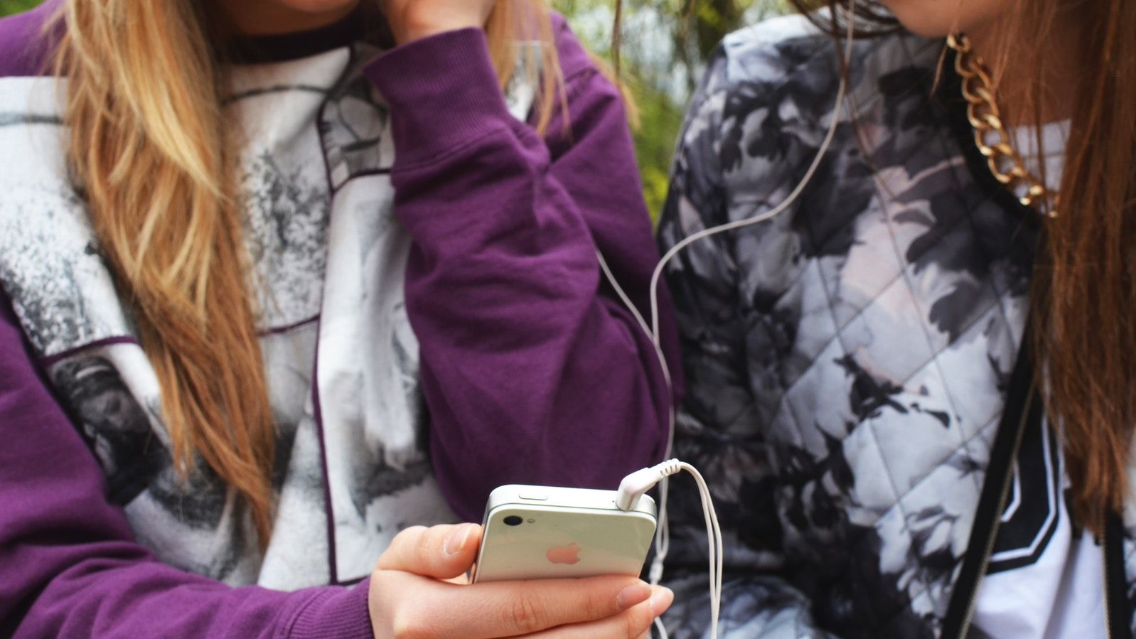 Zwei Teens mit Smartphone hoeren gemeinsam Musik mit Kopfhoerern