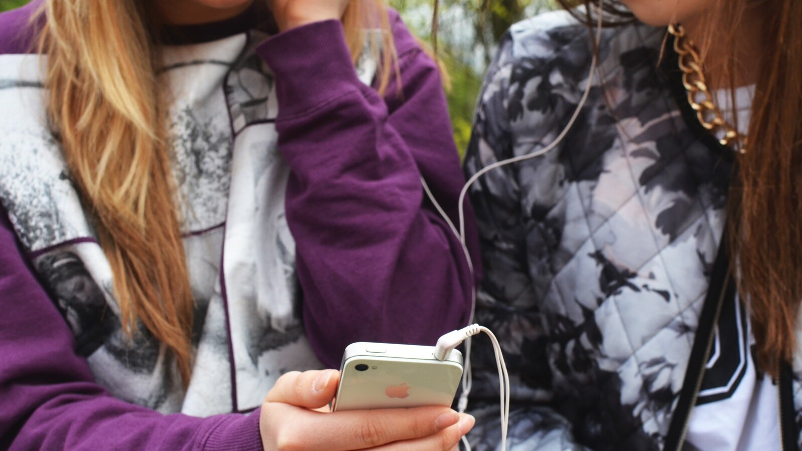 Zwei Teens mit Smartphone hoeren gemeinsam Musik mit Kopfhoerern