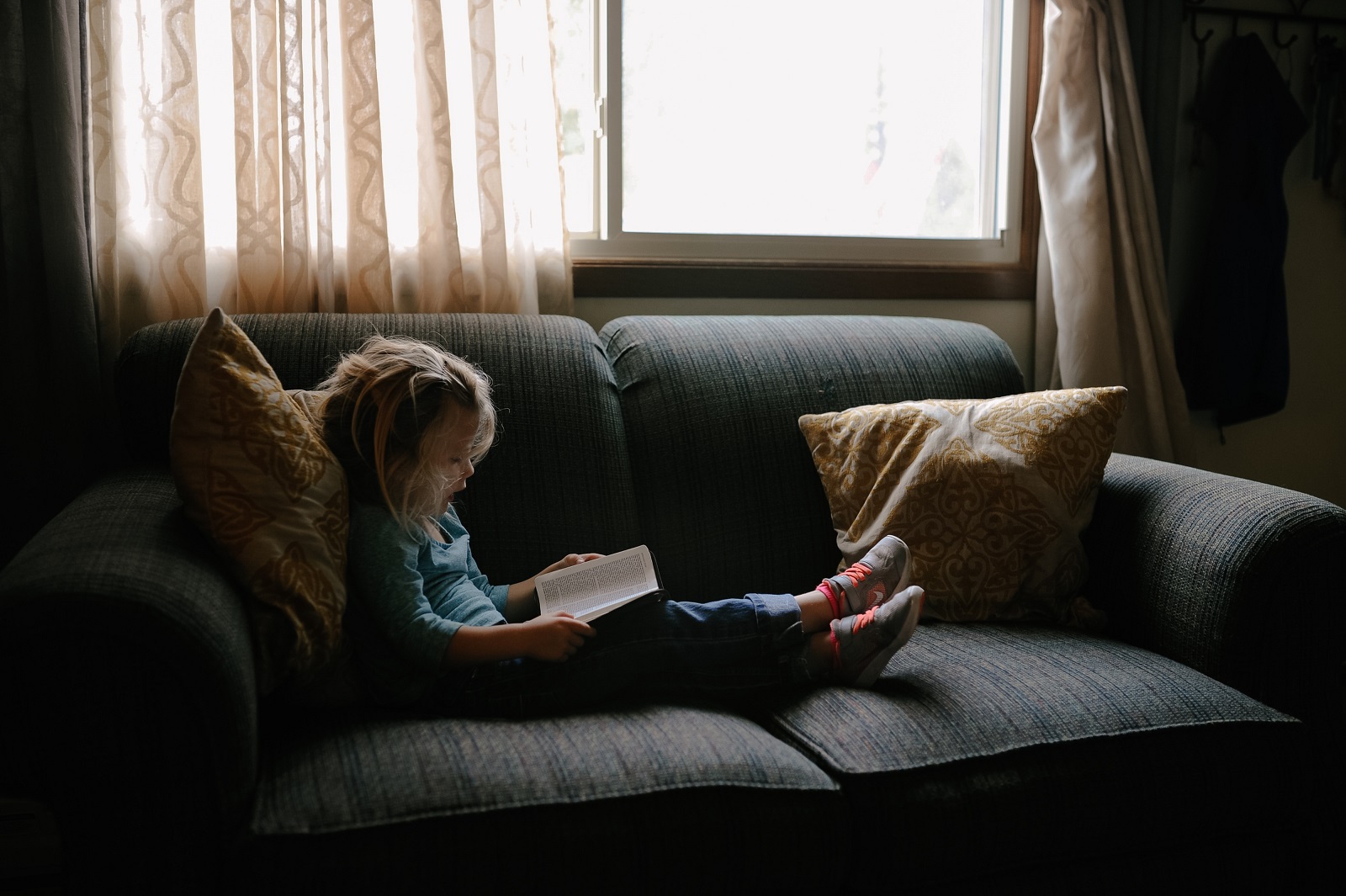 Ein kleines Mädchen liegt auf der Couch und liest ein Buch