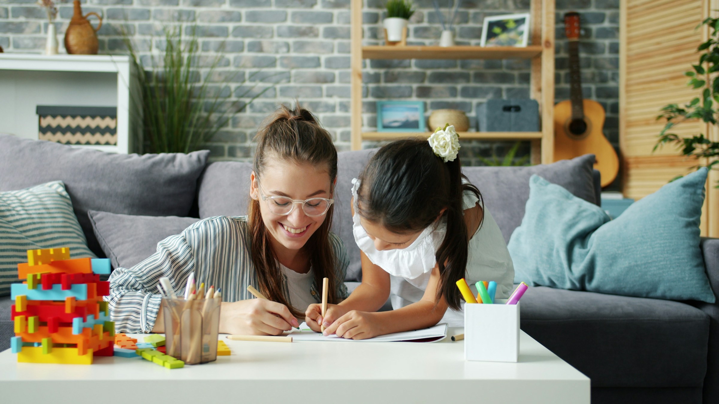 Eine Frau und ein Kind sitzen an einem Tisch und malen zusammen mit Buntstiften. Auf dem Tisch steht weiteres Spielzeug.