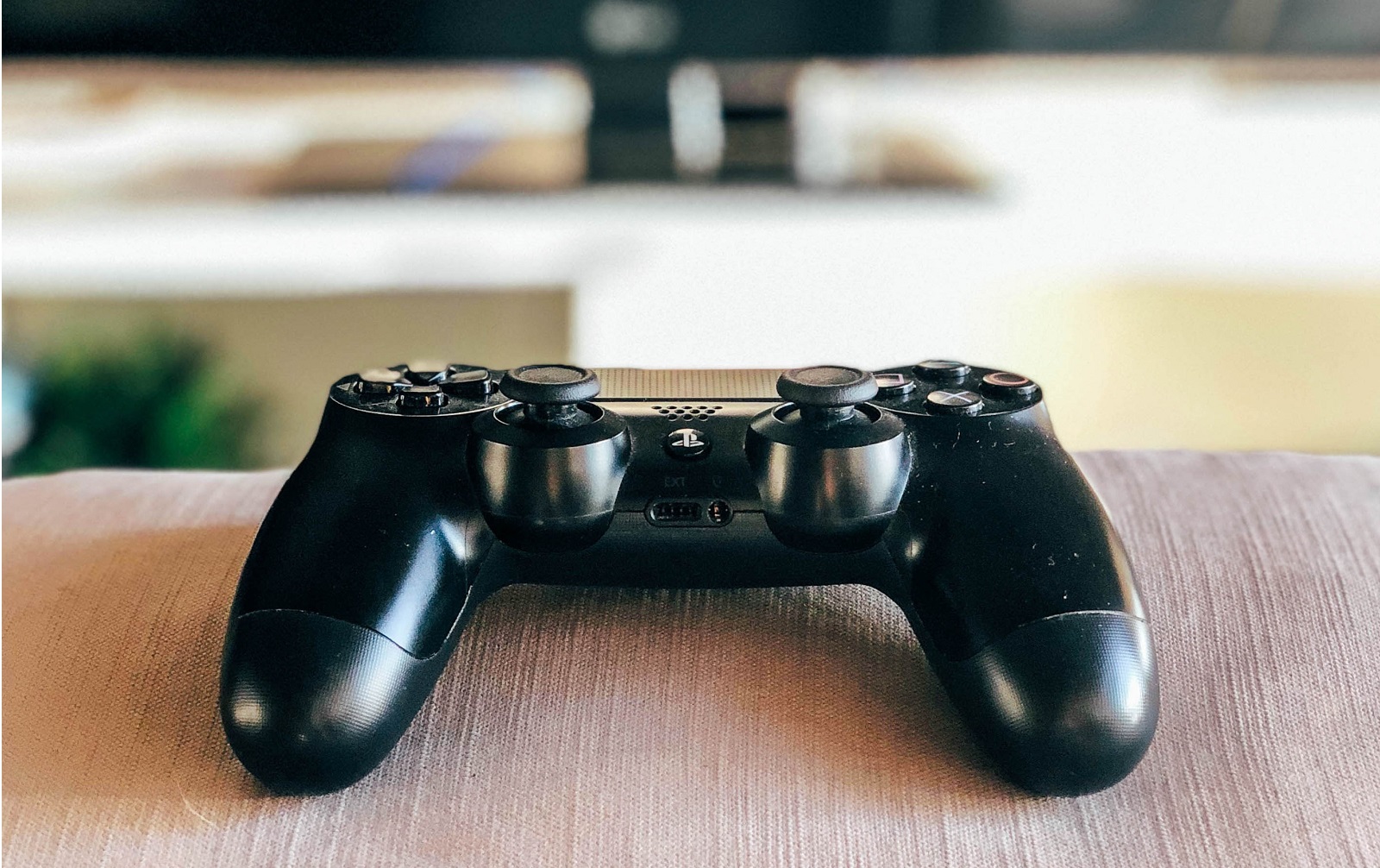 Ein schwarzer Playstationcontroller liegt auf der Couch