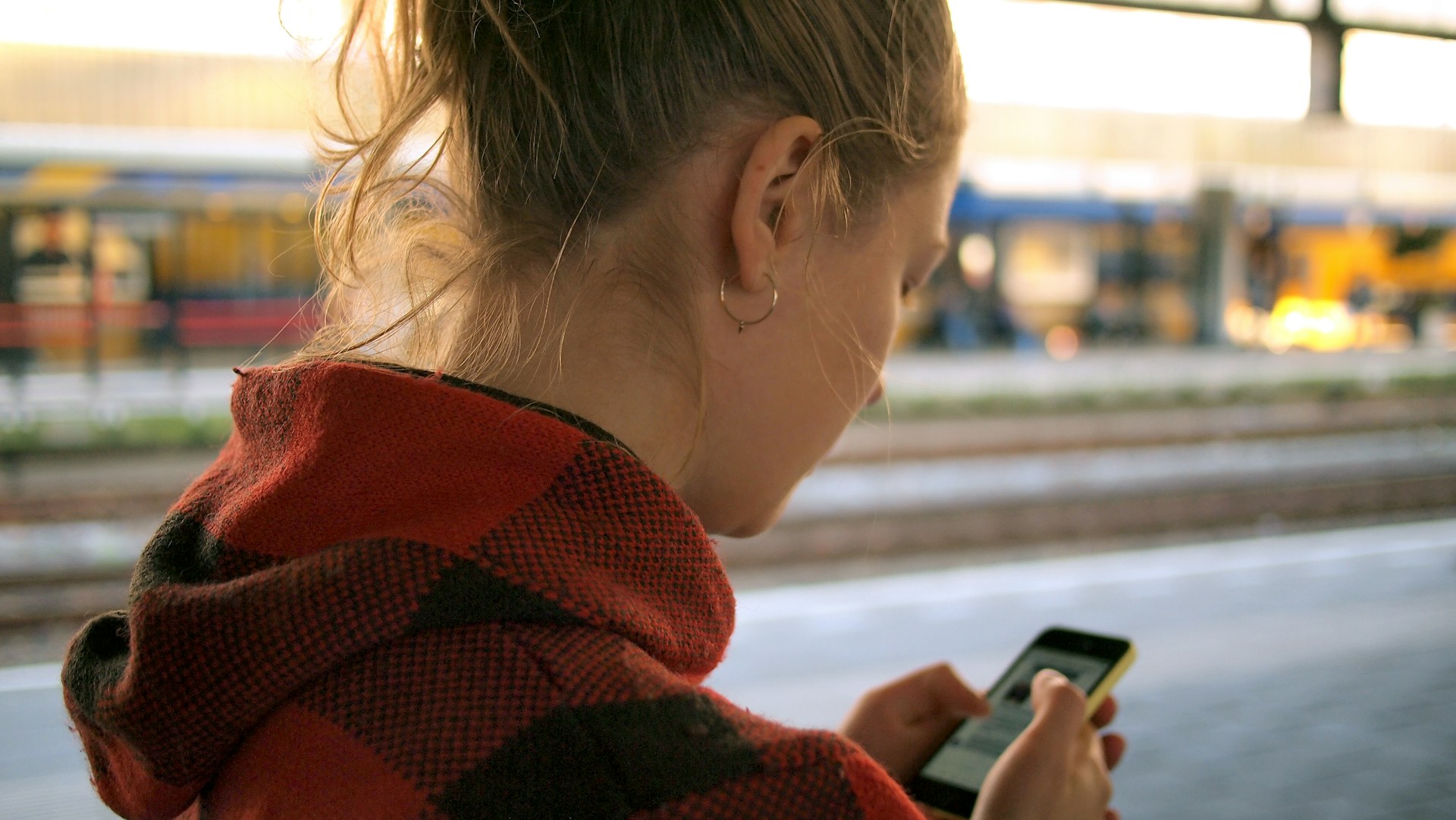 Eine junge Frau steht an einem Bahnsteig und schaut auf ihr Handy.