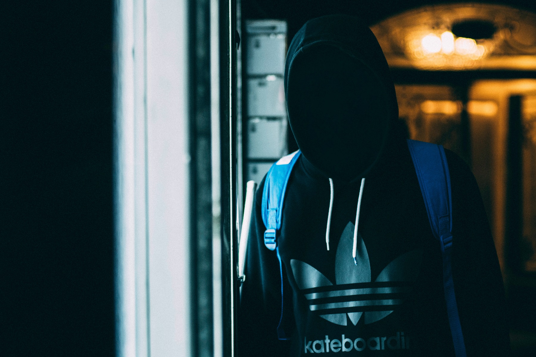 In einem dunklen Raum steht eine Person vorm Fenster, deren Gesicht unter der Kapuze ihres Hoodies nicht zu erkennen ist.