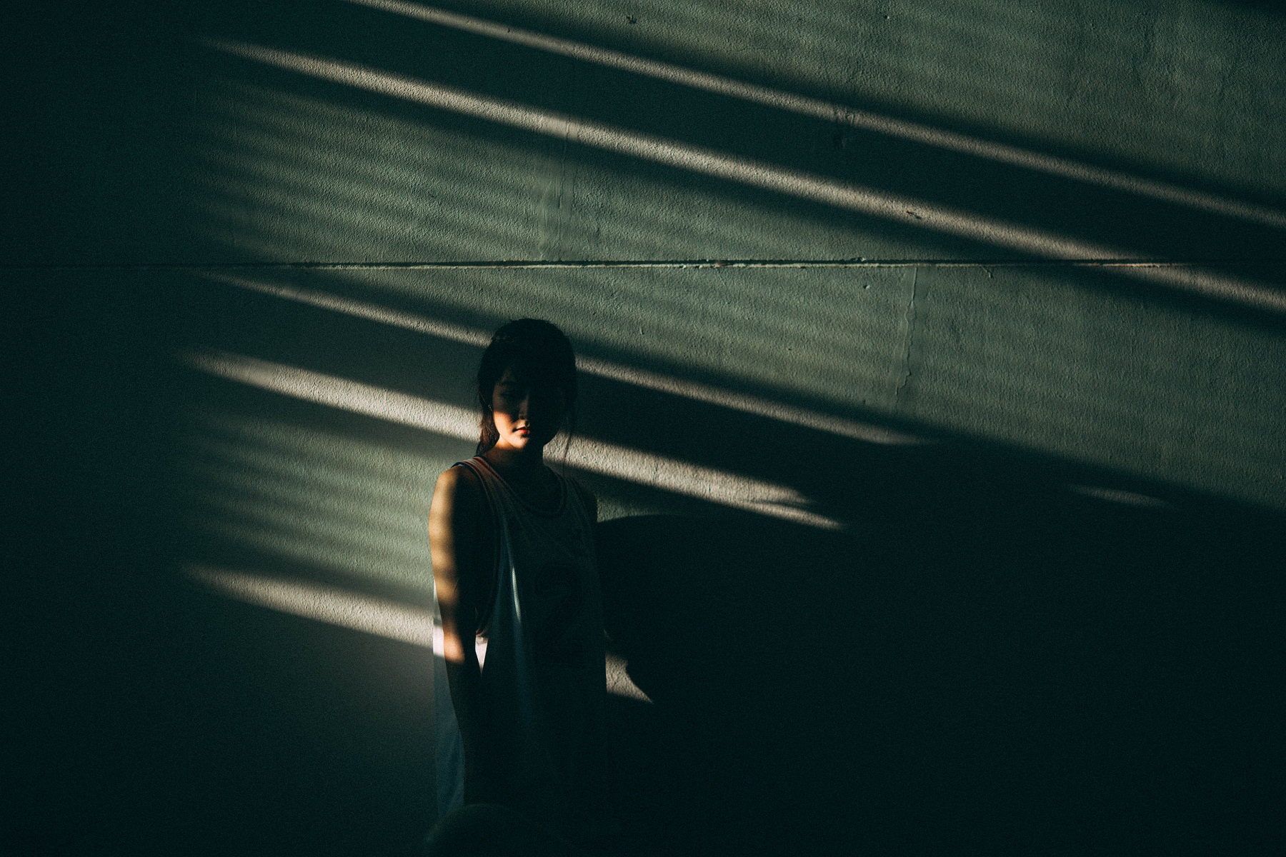 Eine Junge Frau steht an einer Wand, die Sonne wirft Licht und Schatten auf ihren Körper