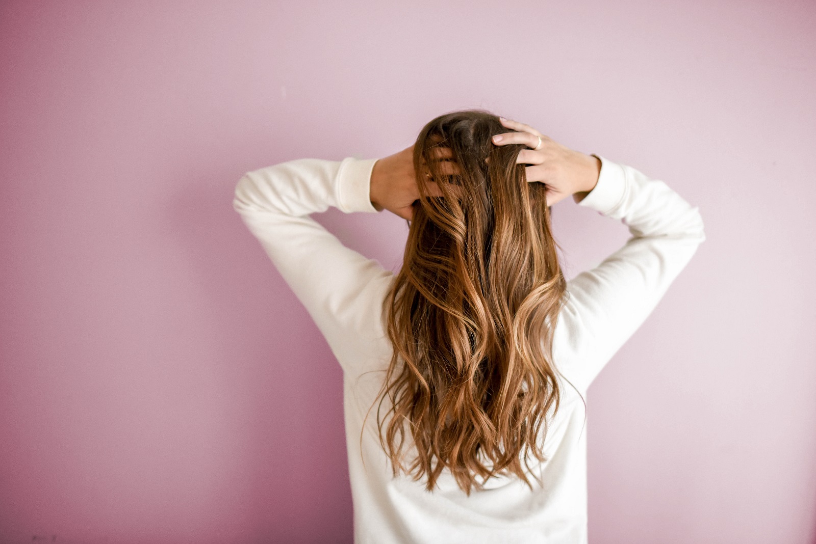 Maedchen fasst sich in lange Haare vor rosa Wand