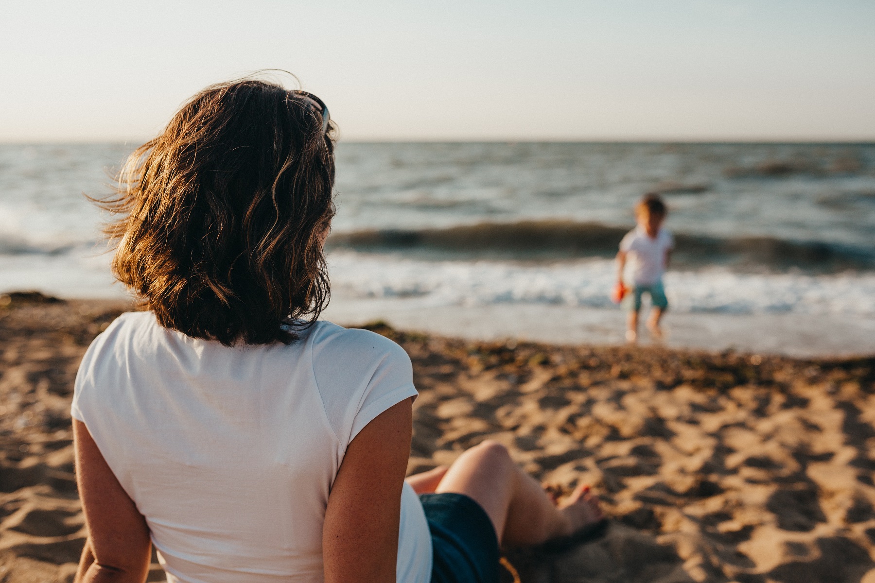 Eine Mutter sitzt am Strand und beobachtet ihre Sohn beim Spielen am Wasser