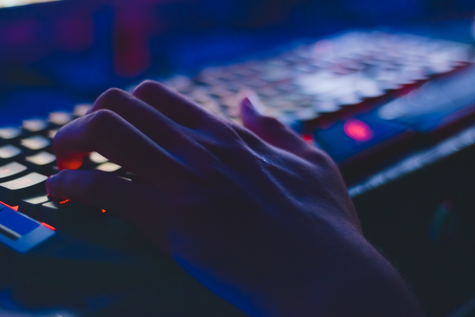 Eine Hand liegt auf einer blau beleuchteten Tastatur.