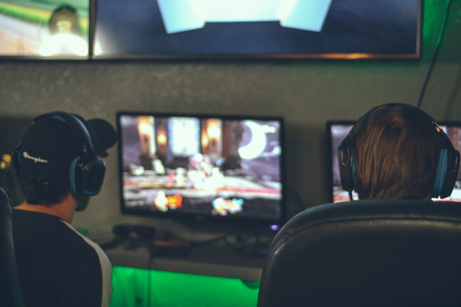 Zwei Jugendliche sitzen vor Bildschirmen und tragen Headsets 