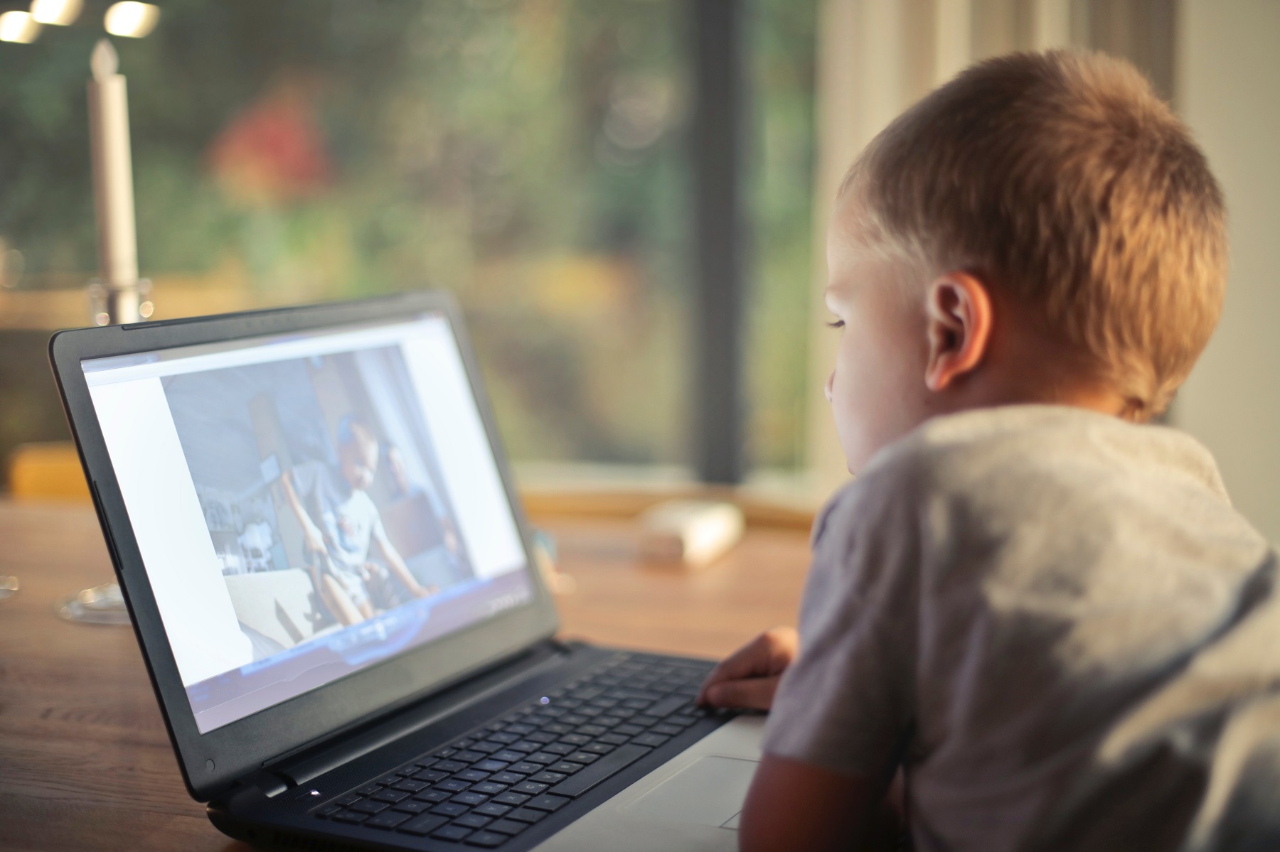 Ein blonder Junge in grauem Shirt sitzt am Tisch und sieht sich auf seinem Laptop einen Film an.
