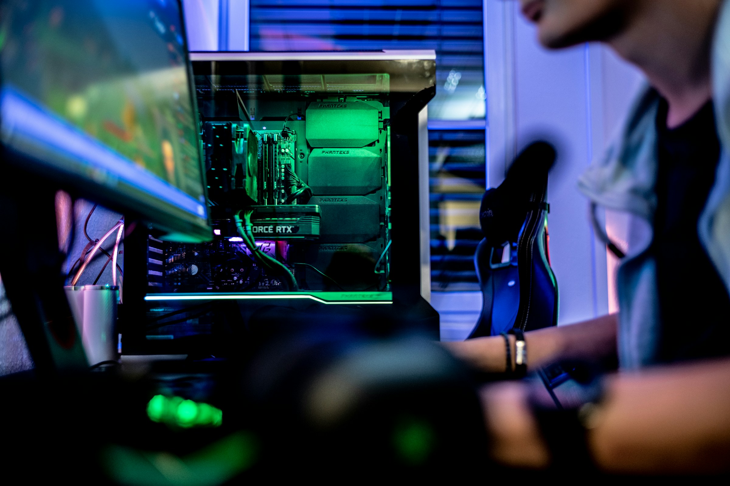 Ein Person sitzt vor einem leuchtenden Gaming-PC an einem Bildschirm.
