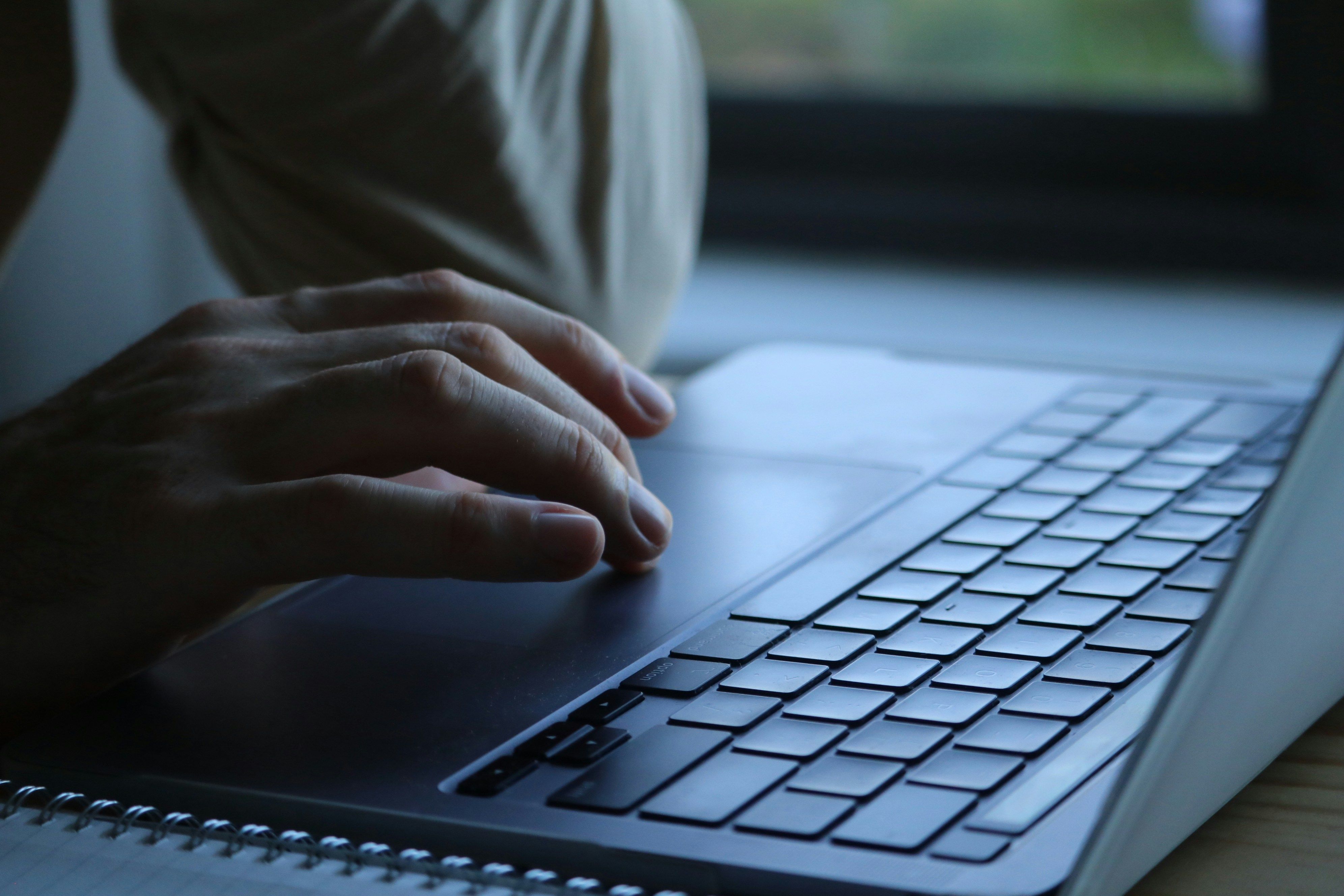 Ein Laptop steht auf einem Tisch, während eine Hand das Touchpad bedient. 
