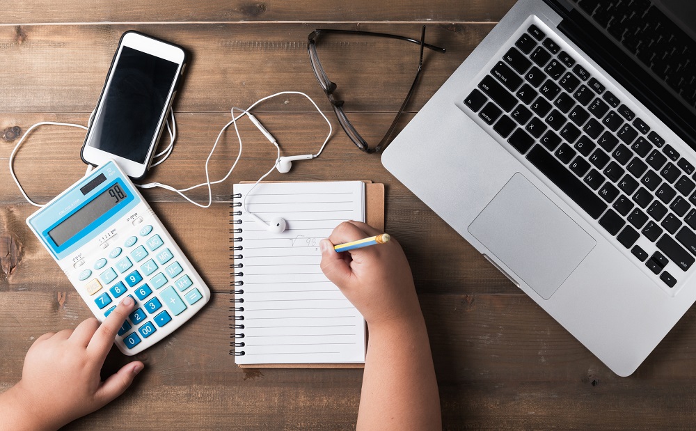 Ein Kind arbeitet am Schreibtisch mit PC, Smartphone und Taschenrechner