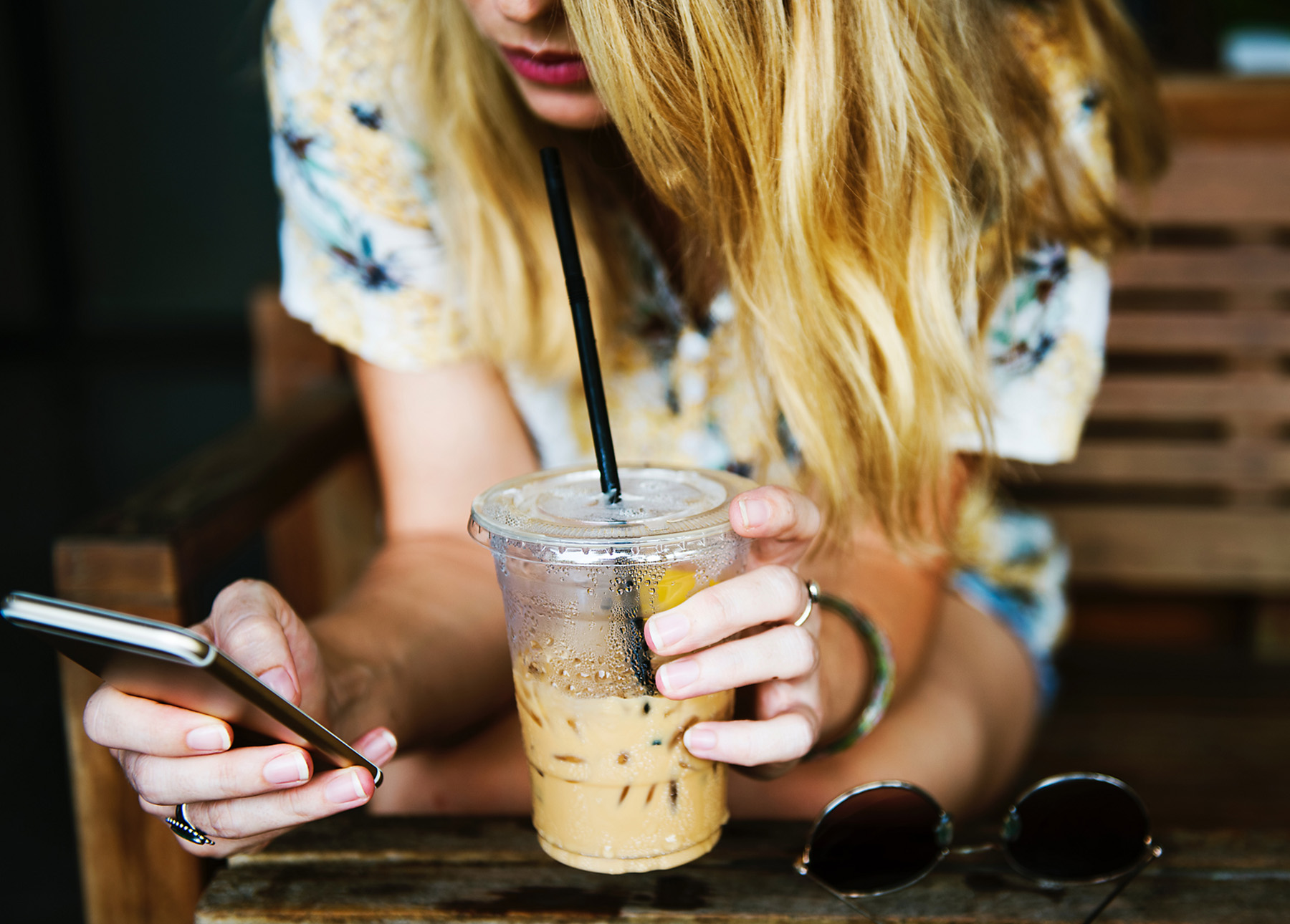 Eine junge Frau hält ein Smartphone und einen Coffee-to-go in den Händen.