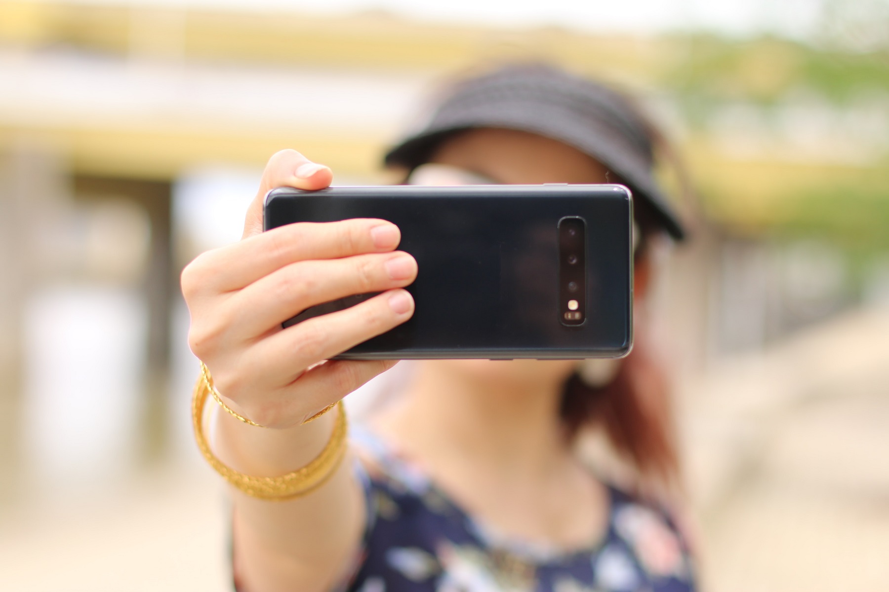 Eine Frau hält sich mit gestrecktem Arm ein schwarzes Smartphone quer vor das Gesicht.