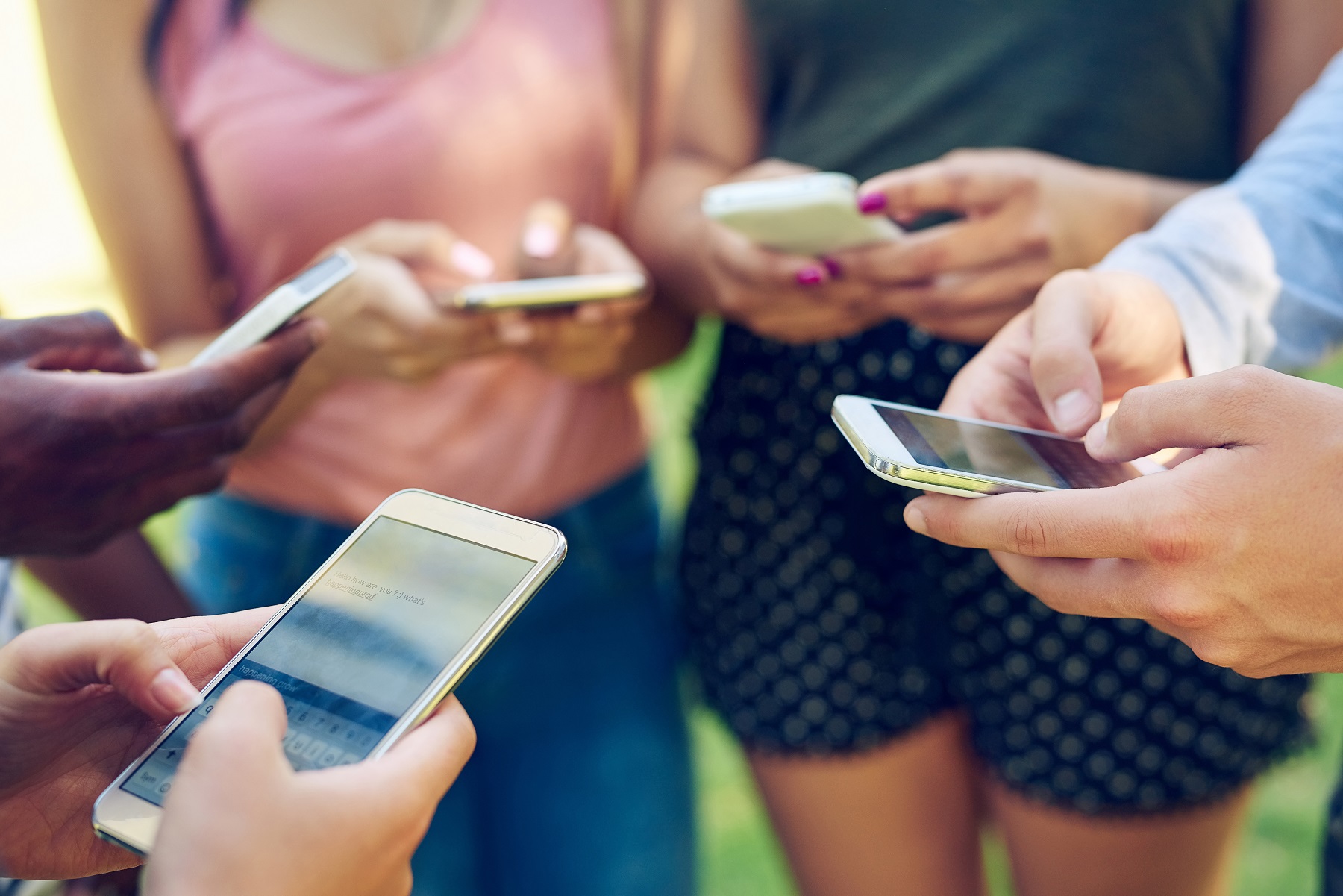 Eine Gruppe junger Leute steht im Kreis und tippt auf Smartphones.