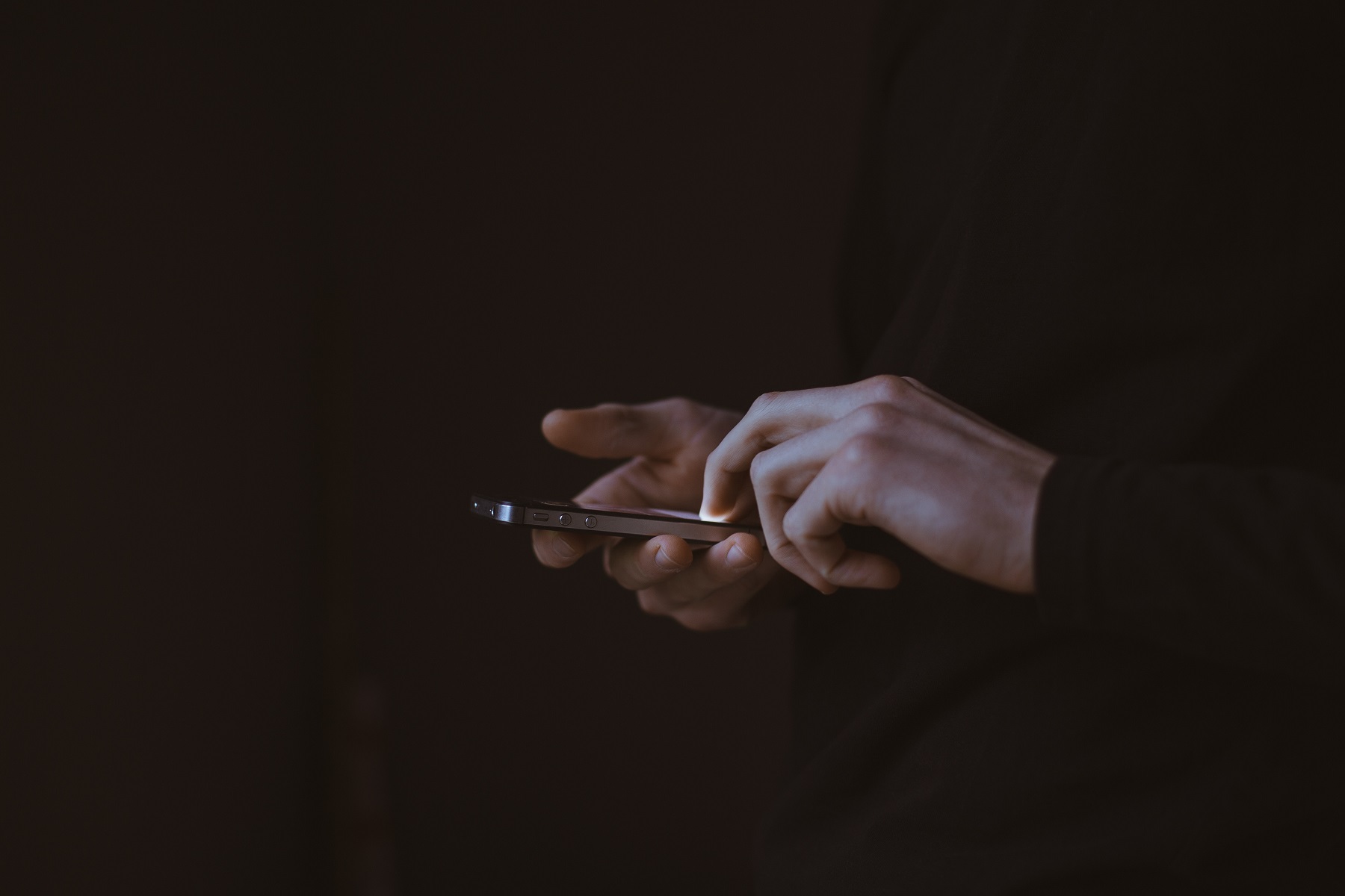 Ein Smartphone wird von zwei Händen gehalten, der Hintergrund ist dunkel.