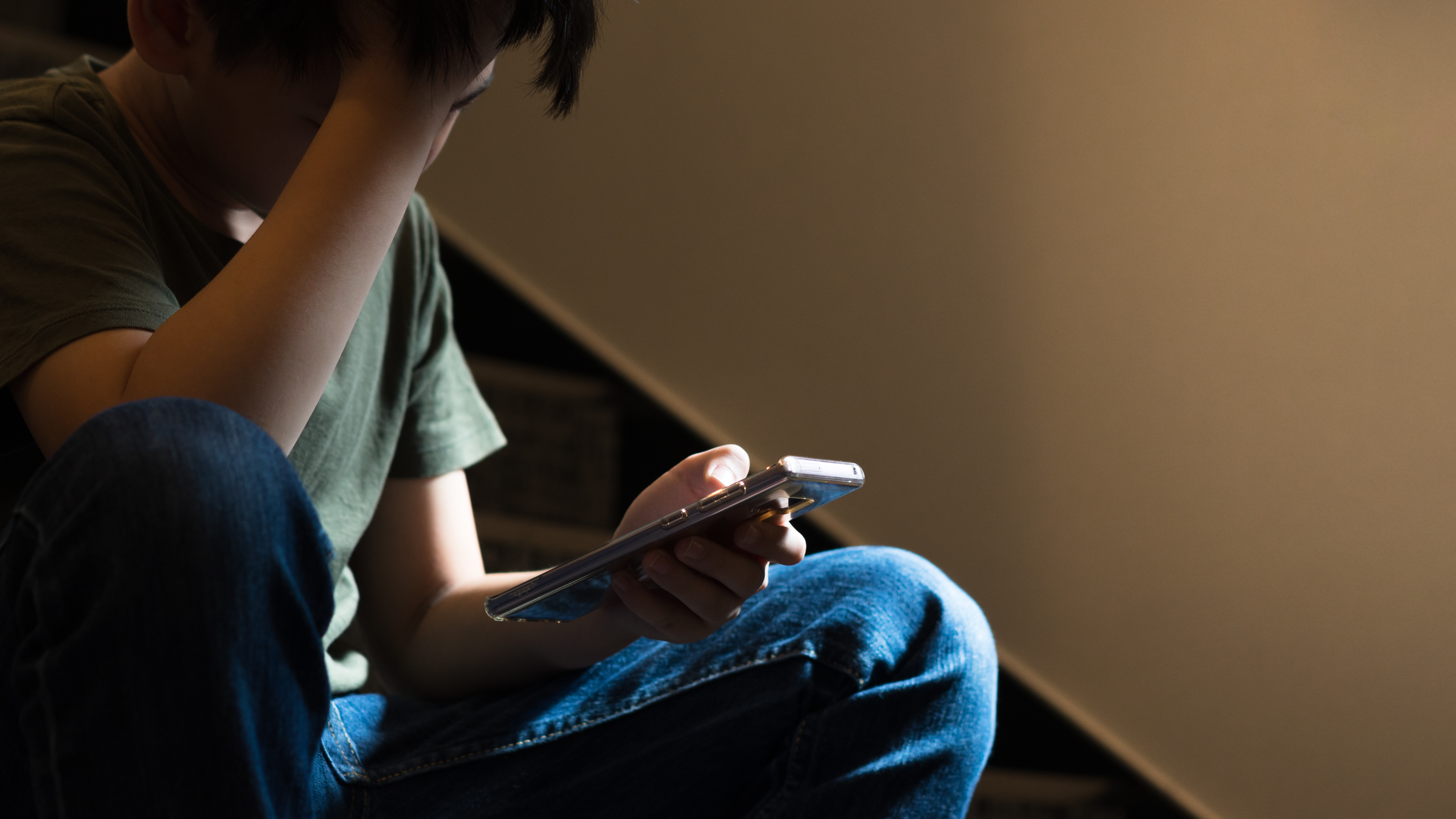 Hunge mit Smartphone in der Hand stützt seinen Kopf mit der Hand.