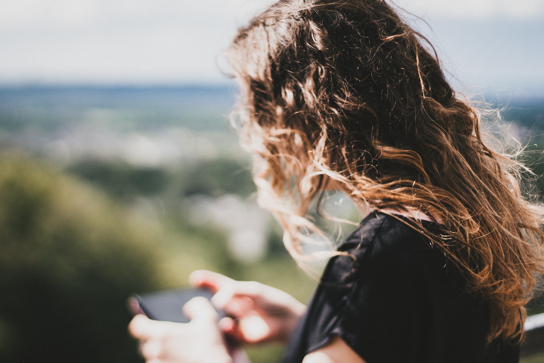 Eine junge Frau mit langen Haaren und Smartphone von hinten