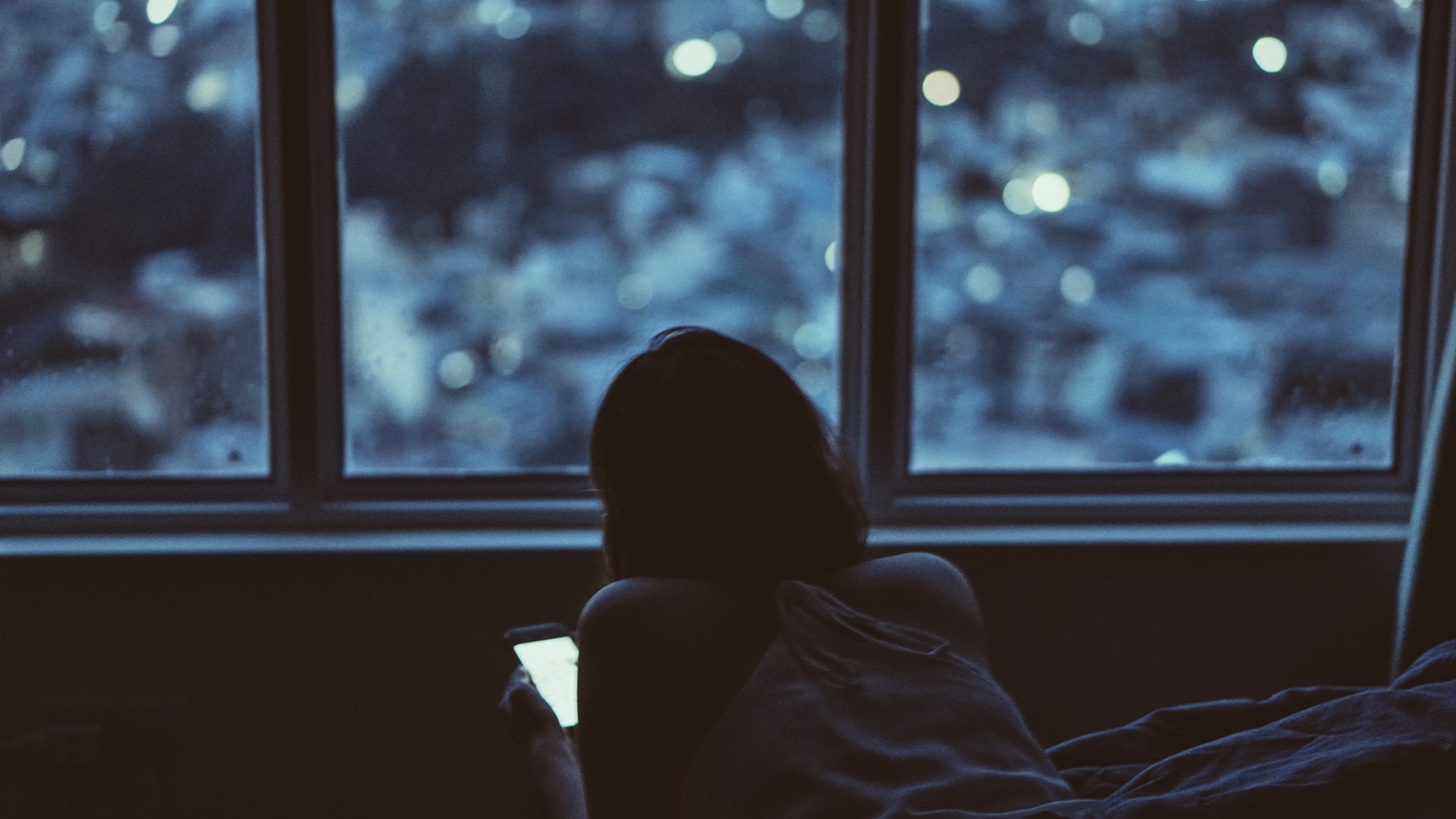 Ein Maedchen sitzt in einem dunklen Zimmer und schaut auf ihr Smartphone