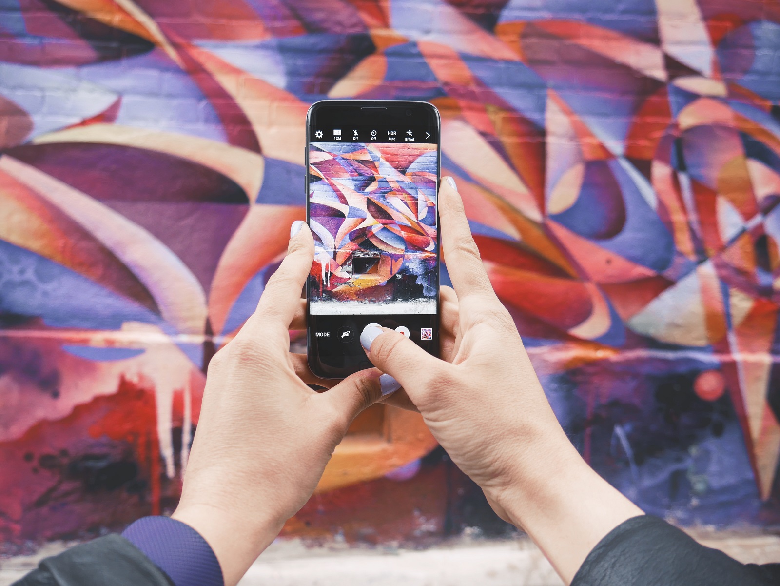 Eine Person hält ein Smartphone vor sich, während sie eine bunte Wand fotografiert
