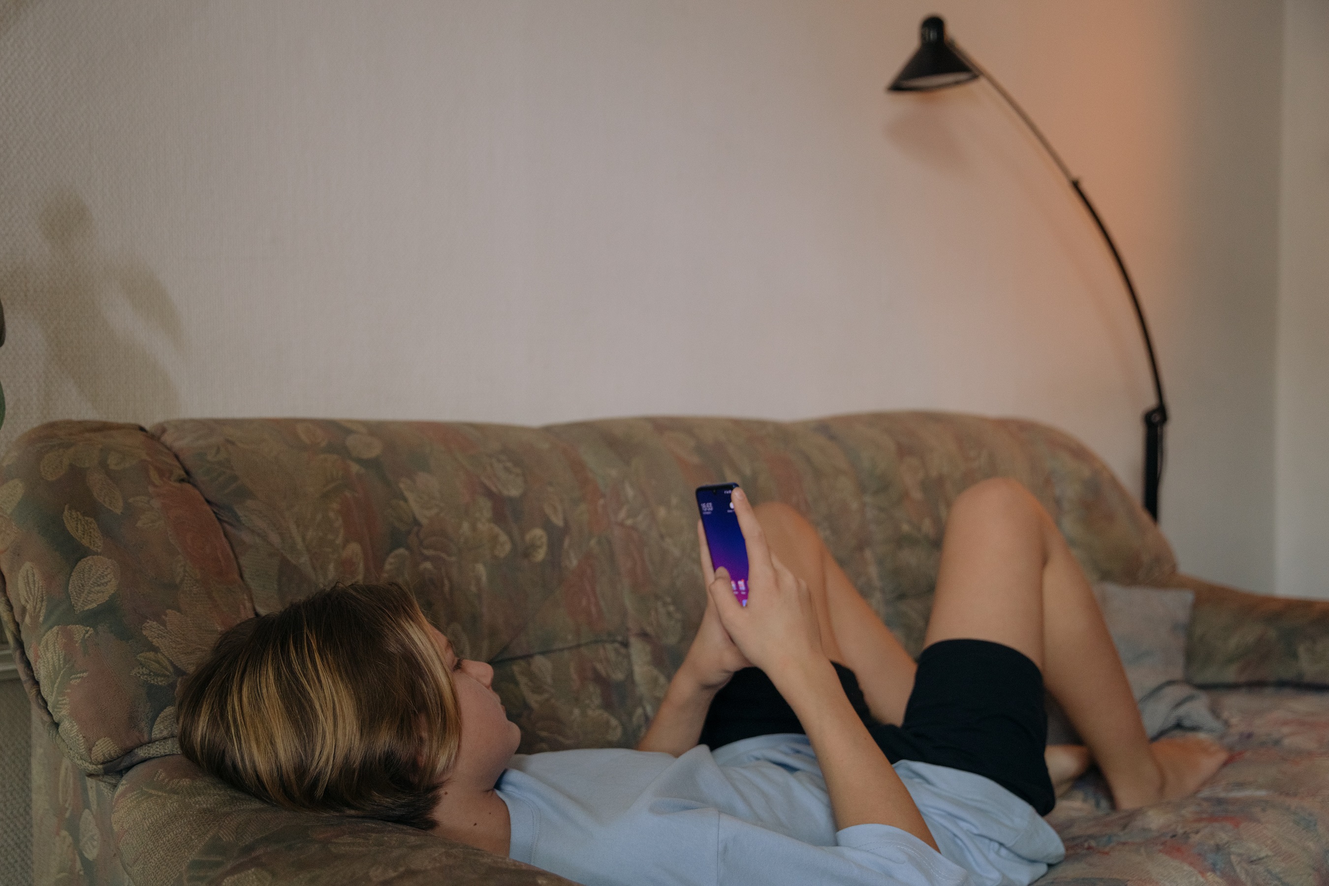 Ein Teenager liegt mit einem Smartphone in der Hand auf dem Sofa. 