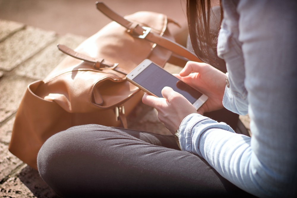 Eine Frau sitzt und haelt ein Smartphone in der Hand