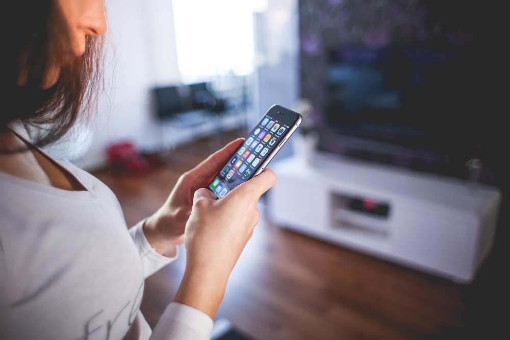 Eine Frau steht mit einem Smartphone vor einem Fernseher
