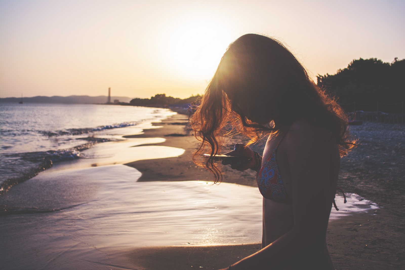 Maedchen am Strand mit dem Smartphone in der Hand.