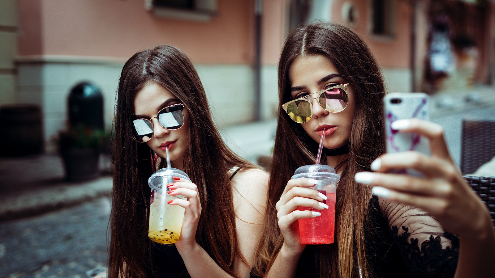 Zwei Maedchen trinken einen Milchshake und nehmen ein Selfie auf.